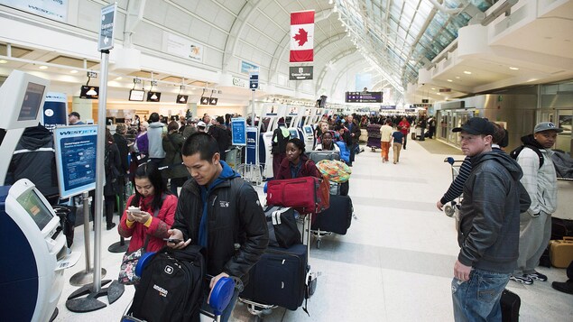 Des personnes font la file devant des bornes à l'aéroport Pearson de Toronto.