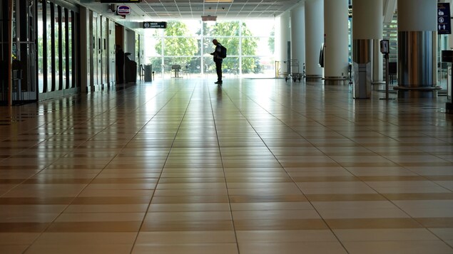 Un homme debout seul dans un grand couloir lumineux.