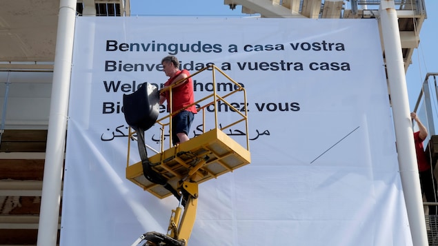 Un volontaire de la Croix-Rouge installe une immense affiche où il est inscrit, dans plusieurs langues différentes, « Bienvenue chez vous ». Un volontaire de la Croix-Rouge installe une immense affiche où il est inscrit, dans plusieurs langues différentes, « Bienvenue chez vous ».