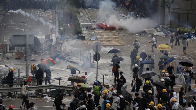Dans une rue aux allures apocalyptiques, les manifestants éparses affrontent une rangée de policiers. Autour, des gaz flottent dans les airs.