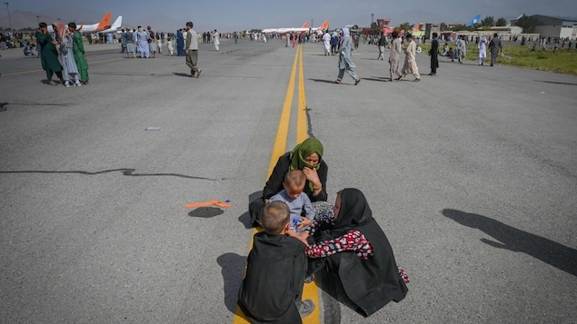 Afghan people sit along the tarmac as they wait to leave the Kabul airport.