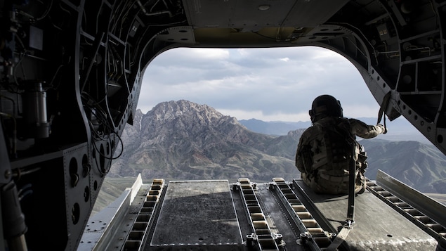 Un militaire américain regarde des montagnes à partir d'un hélicoptère Chinook.