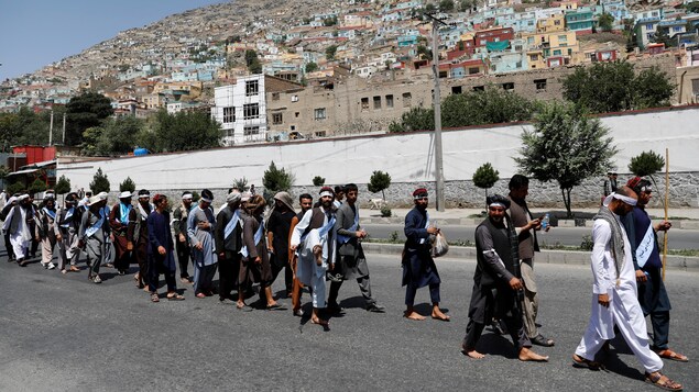 Des dizaines d'Aghans marchent dans une rue pavée de Kaboul. 