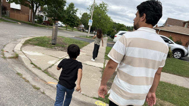 Le père et ses deux enfants traversent une rue résidentielle.