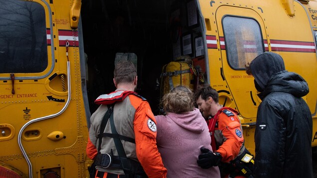 Deux membres de l'Aviation royale canadienne aident une femme à monter à bord d'un hélicoptère.