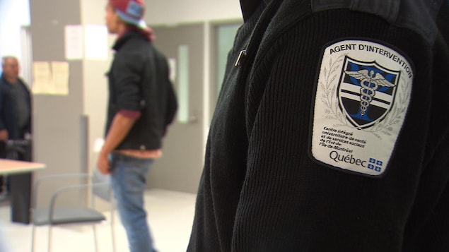 un jeune homme dans une institution avec un agent, dont l’écusson indique qu'il est un agent d'intervention.
