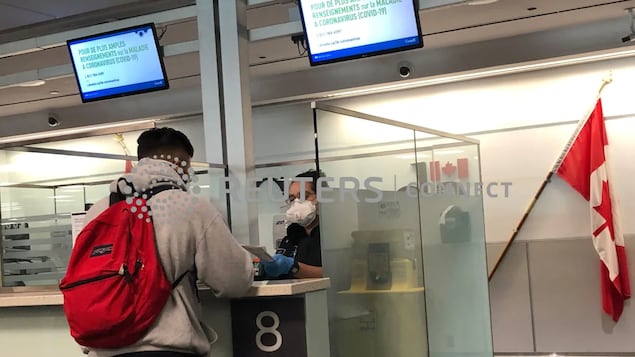 Une agente de l'ASFC portant un masque de protection vérifie le passeport d’un passager.