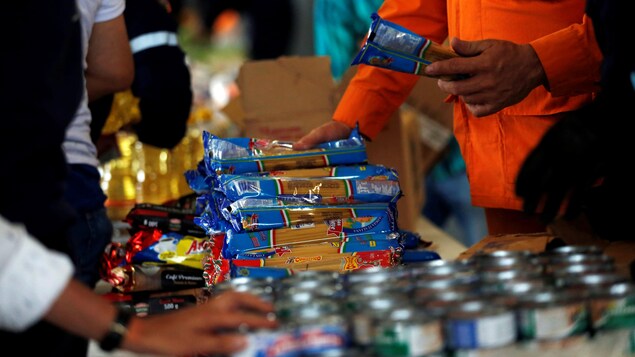 Des travailleurs empilent des paquets de pâtes alimentaires et des cannes de nourriture sur des tables.