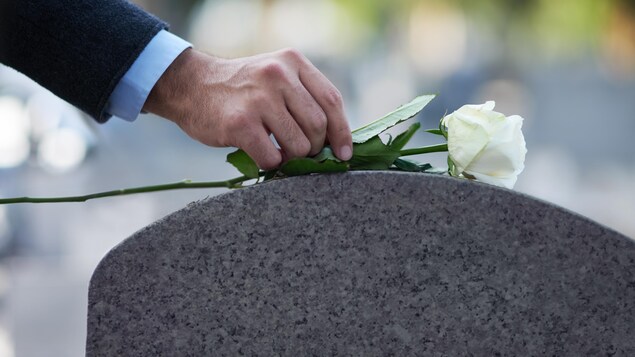 Un homme dépose une rose blanche sur le dessus d'une pierre tombale lors de funérailles.