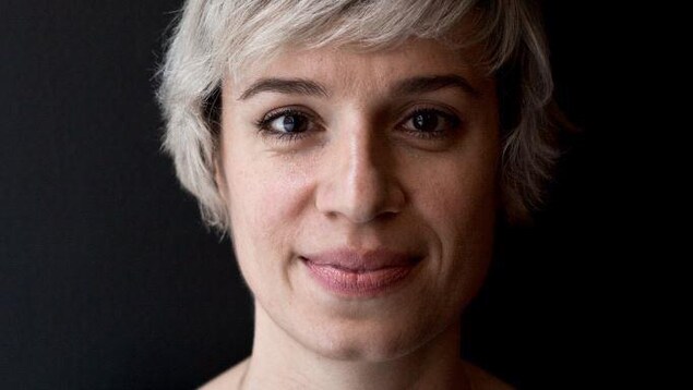 Portrait en couleur sur fond noir de l'autrice Aimée Lévesque. La jeune femme sourit, bouche fermée. Elle a les cheveux blonds courts.