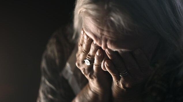 Une personne âgée désespérée pleure dans une pièce sombre.