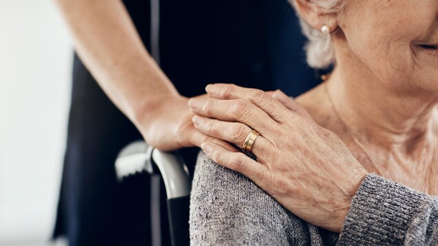 Une dame âgée sur un fauteuil roulant avec une personne debout.