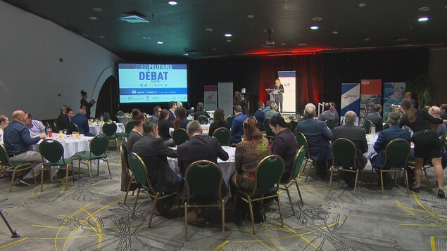 Des gens d'affaires assis à des tables écoutent une conférencière.