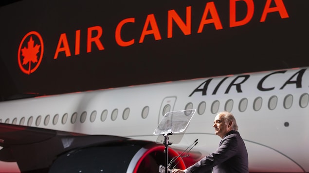 Calin Rovinescu parle derrière un lutrin posé devant un avion Airbus A220-300.
