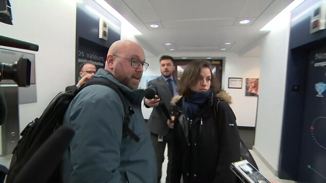 Un homme et une femme entourés de journalistes.