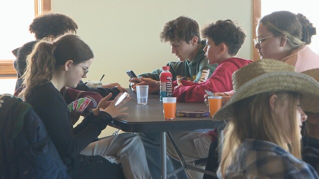 Des jeunes assis autour d'une table dont certains regardent leurs cellulaires le 1er avril 2023 à Lumsden en Saskatchewan.