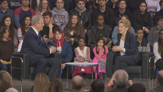 Photo d'Al Gore et de Kathleen Wynne assis dans des fauteuils sur un plateau devant des étudiants. Photo d'Al Gore et de Kathleen Wynne assis dans des fauteuils sur un plateau devant des étudiants.