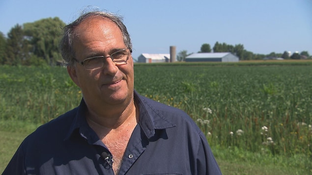 Un homme devant l'étendue d'un champ et de sa ferme.