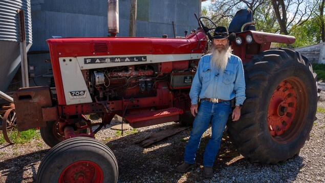 Un homme portant un chapeau de cowboy devant un tracteur sur une ferme.