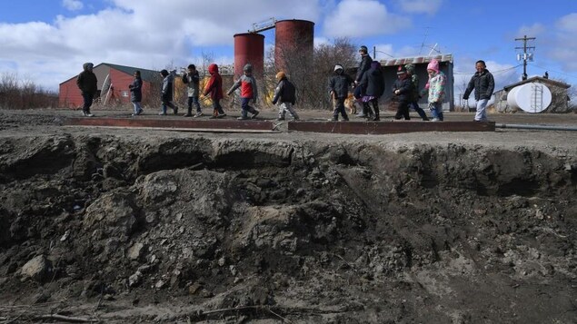 A group of children walk along an eroded road. 