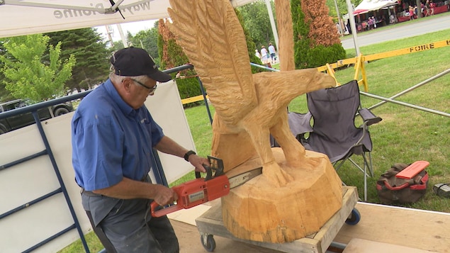 Un homme âgé avec une scie mécanique taille un aigle dans du bois. 