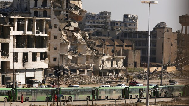 Plusieurs autobus verts sont stationnés devant un immeuble en ruine dans la ville syrienne d'Alep. Plusieurs autobus verts sont stationnés devant un immeuble en ruine dans la ville syrienne d'Alep.