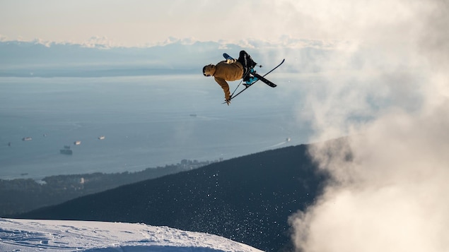 Durant un saut, il agrippe l'un de ses skis dans les airs.