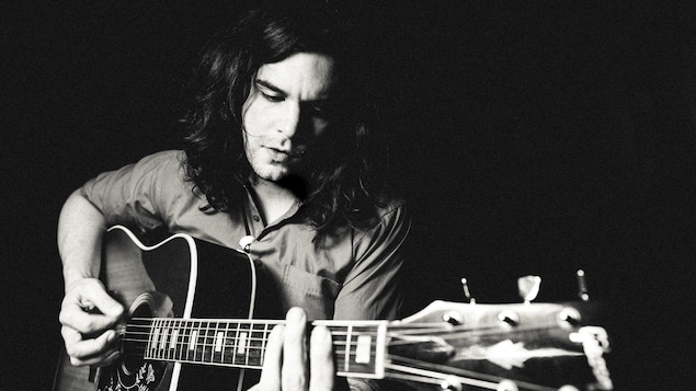 Un homme plongé dans la pénombre joue de la guitare.
