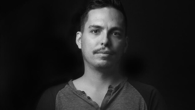 Portrait en noir et blanc, sur fond noir, d'Alex Noël. Le jeune homme porte une moustache.