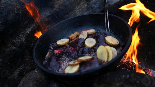 Une casserole posée sur un feu, dans laquelle cuisent des pommes de terre et de la viande.