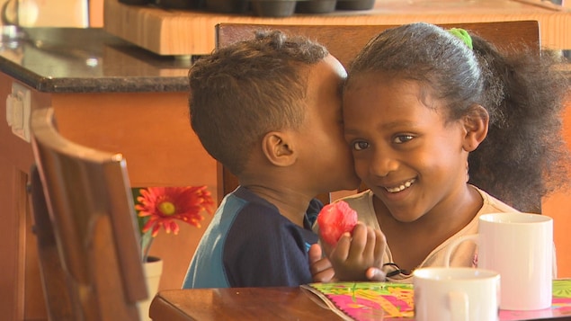 Une fillette sourit, une fraise à la main, pendant qu'un enfant lui murmure quelque chose à l'oreille. Une fillette sourit, une fraise à la main, pendant qu'un enfant lui murmure quelque chose à l'oreille.