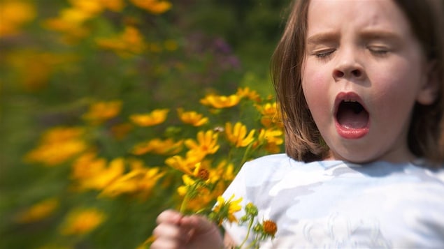 Une fillette éternue devant des fleurs.
