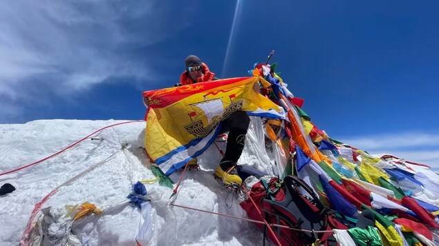 Rick Irvine ajoute le drapeau aux autres déjà attachés à un piquet au sommet de la montagne.