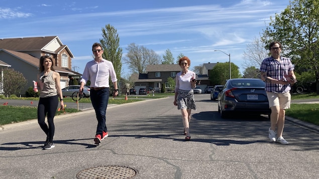 Deux femmes et deux hommes marchent dans une rue de banlieue par une journée ensoleillée d'été avec des dépliants dans les mains.