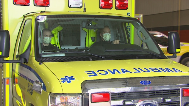 Des ambulanciers portent un masque dans leur véhicule.