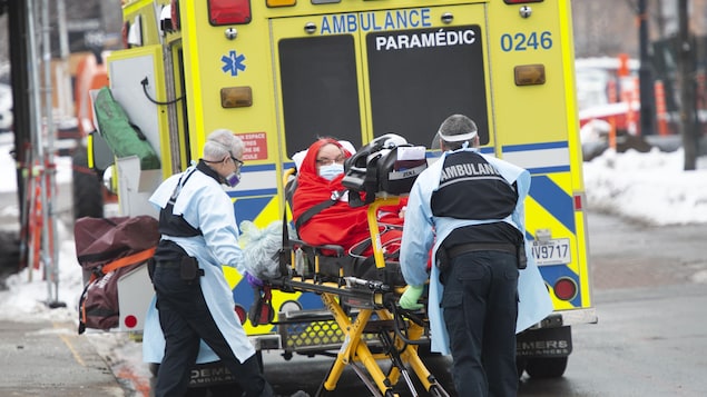 Un patient est transporté sur une civière vers une ambulance par deux ambulanciers.