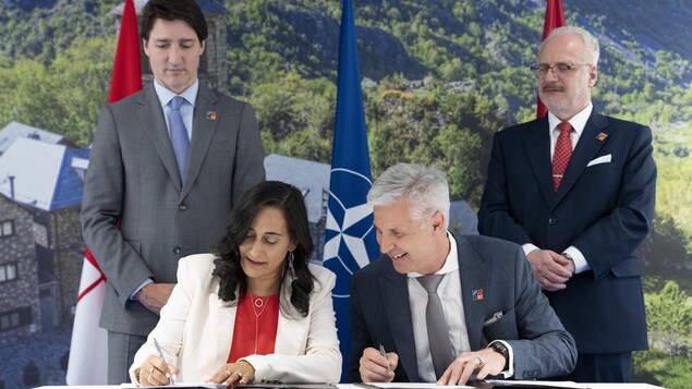 Mme Anand et M. Pabriks, assis, signent des documents. MM. Trudeau et Levits observent la scène.