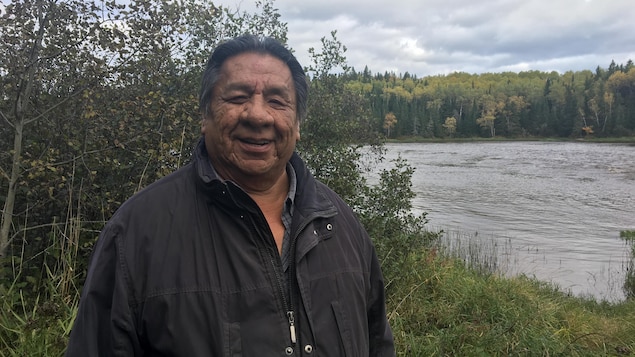 Un Autochtone sourit à la caméra, au bord d'une rivière.