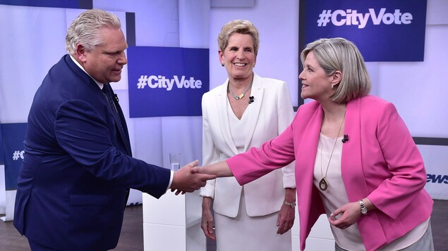 Doug Ford serre la main à Andrea Horwath pendant que Wynne les regarde en souriant. Doug Ford serre la main à Andrea Horwath pendant que Wynne les regarde en souriant.