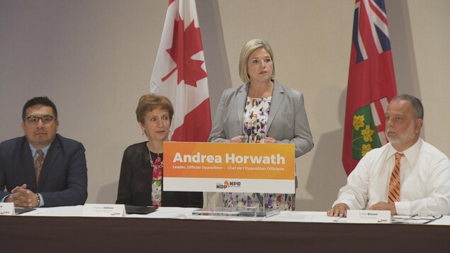 Andrea Horwath debout devant un lutrin avec à ses côté, assis, trois députés. Andrea Horwath debout devant un lutrin avec à ses côté, assis, trois députés.