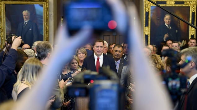 Les députés conservateurs sont serrés autour d'Andrew Scheer. À l'avant-plan, quelqu'un prend une photo de la scène.