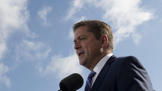 Plan rapproché de M. Scheer devant un ciel bleu ponctué de petits nuages blancs.