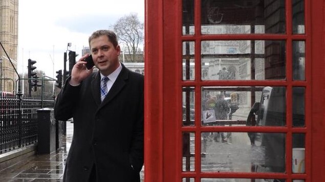 Andrew Scheer parle au cellulaire adossé à une cabine téléphonique rouge à Londres.