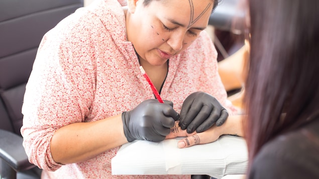 Angela Hovak Johnston tatouant la main d'une femme inuk selon la technique traditionnelle
