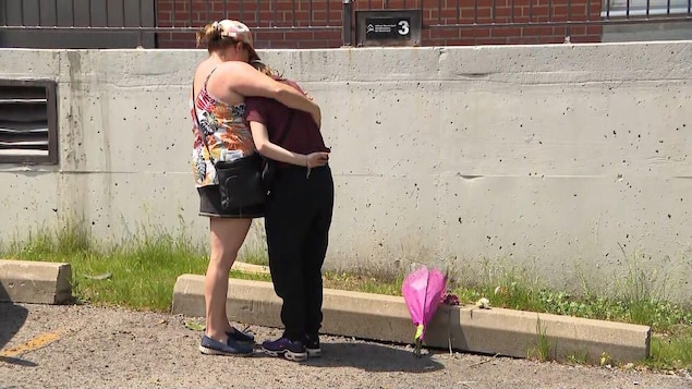 A woman holds her teenage daughter in her arms, with the flowers they brought at their feet.