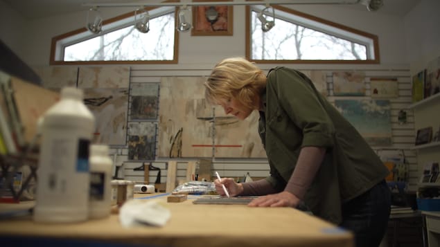 Anne Brochu Lambert dans son atelier penchée sur une tablette, un stylet à la main.