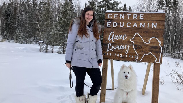 Anne Lemay se tient debout à côté d'un pancarte indiquant le nom Centre Éducanin. À ses côtés, il y a un chien blanc au bout d'une laisse. 