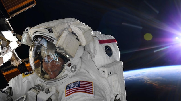 Dans sa combinaison d'astronaute, Anne McClain sourit à la caméra, avec la Terre en arrière-plan.