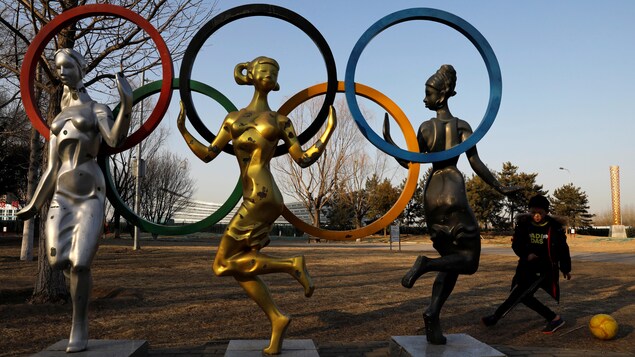 Un garçon joue au ballon près de trois statues surmontées des anneaux olympiques.