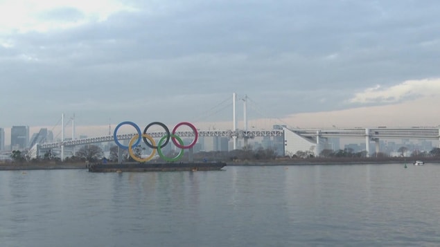 Les cinq anneaux olympiques sont sur une barge devant un grand plan d'eau.
